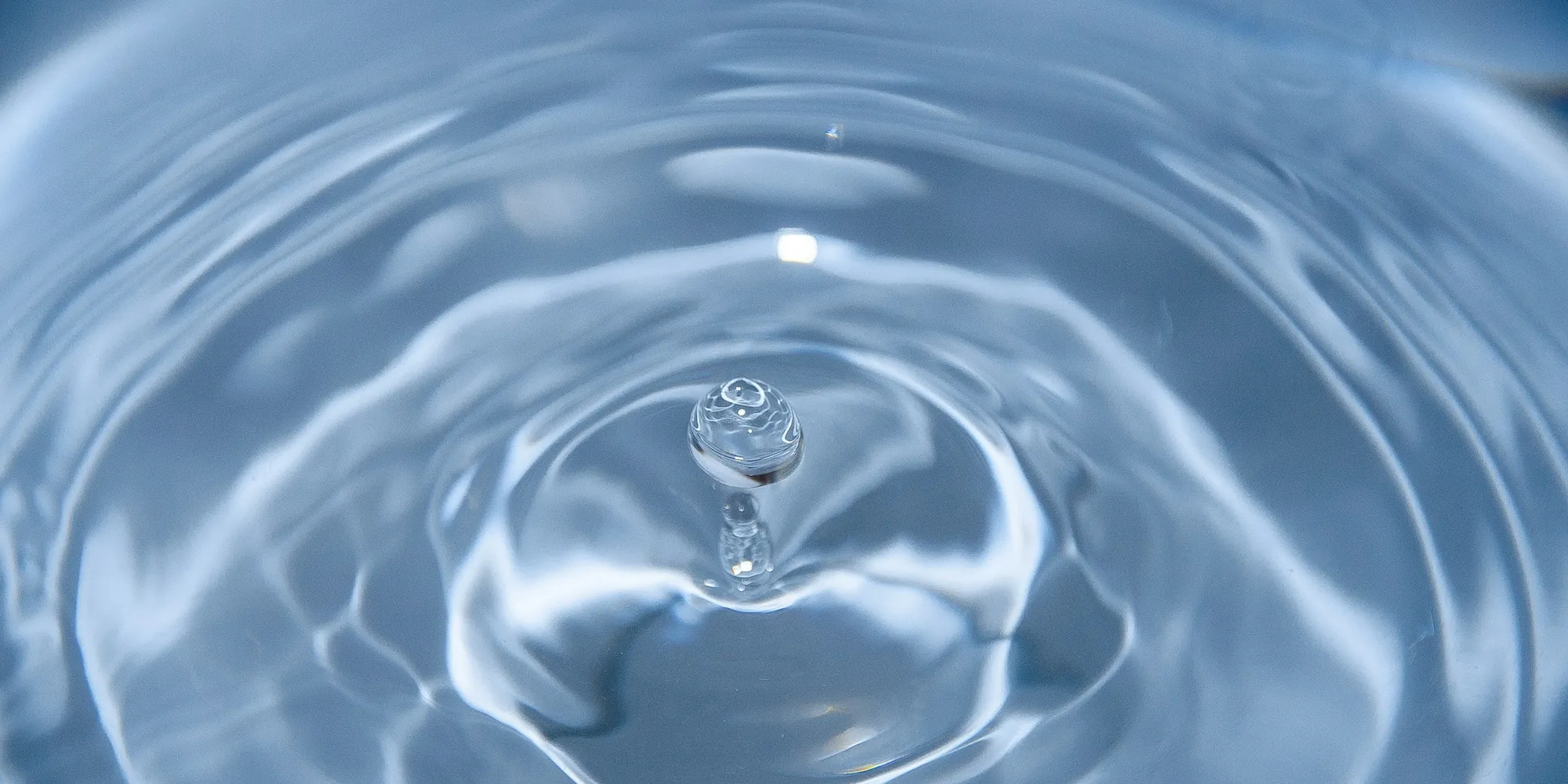 A single drop of water falling into still blue water, sending out ripples